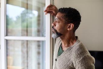Older man gazes outside window, alone in his house