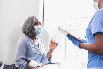 A woman in a mask talking to a doctor holding a chart