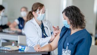 Doctor with mask and face shield administering vaccine to another health care worker