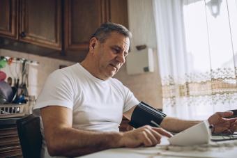 older man checking blood pressure at dining table 