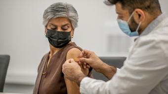 Senior woman getting a flu shot wearing a mask, doctor bandaging her arm