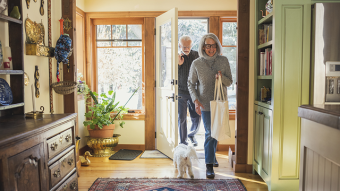 An older couple walking into their home with groceries