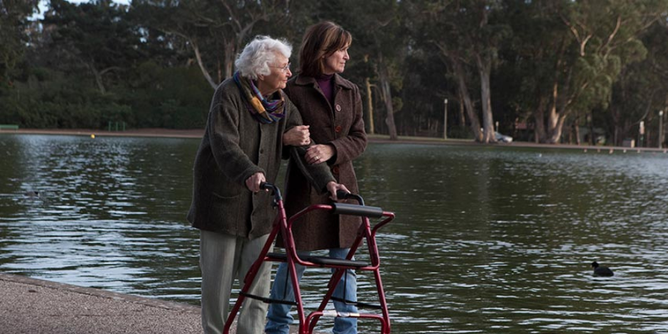An older woman with walker strolling with daughter next to a pond