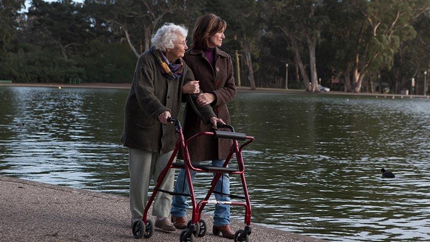 Senior with walker walking with daughter by a pond