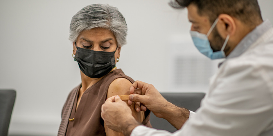 A woman wearing mask getting a vaccine from masked health care worker