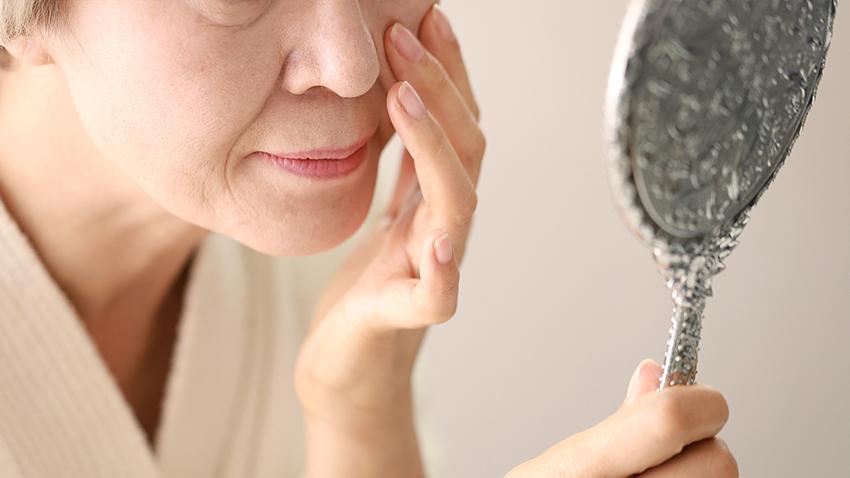 Senior woman checking face in mirror